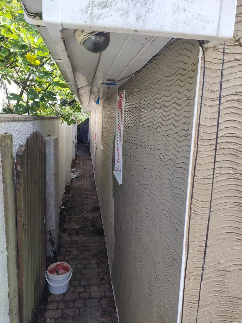 Narrow side passage with the scratch coat of render applied and beads fitted around the windows