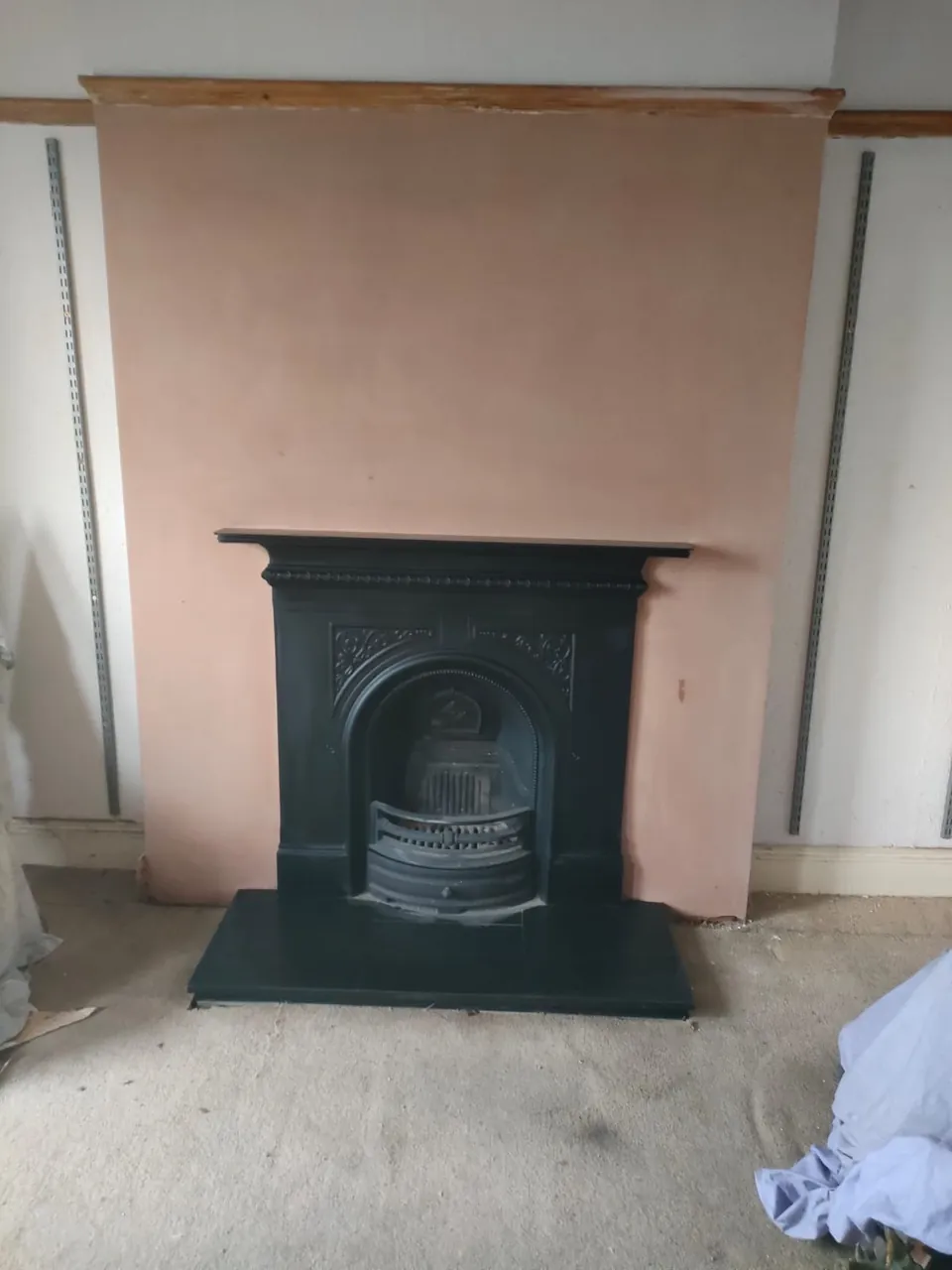 Newly plastered chimney breast around a black cast iron fireplace with a slate hearth