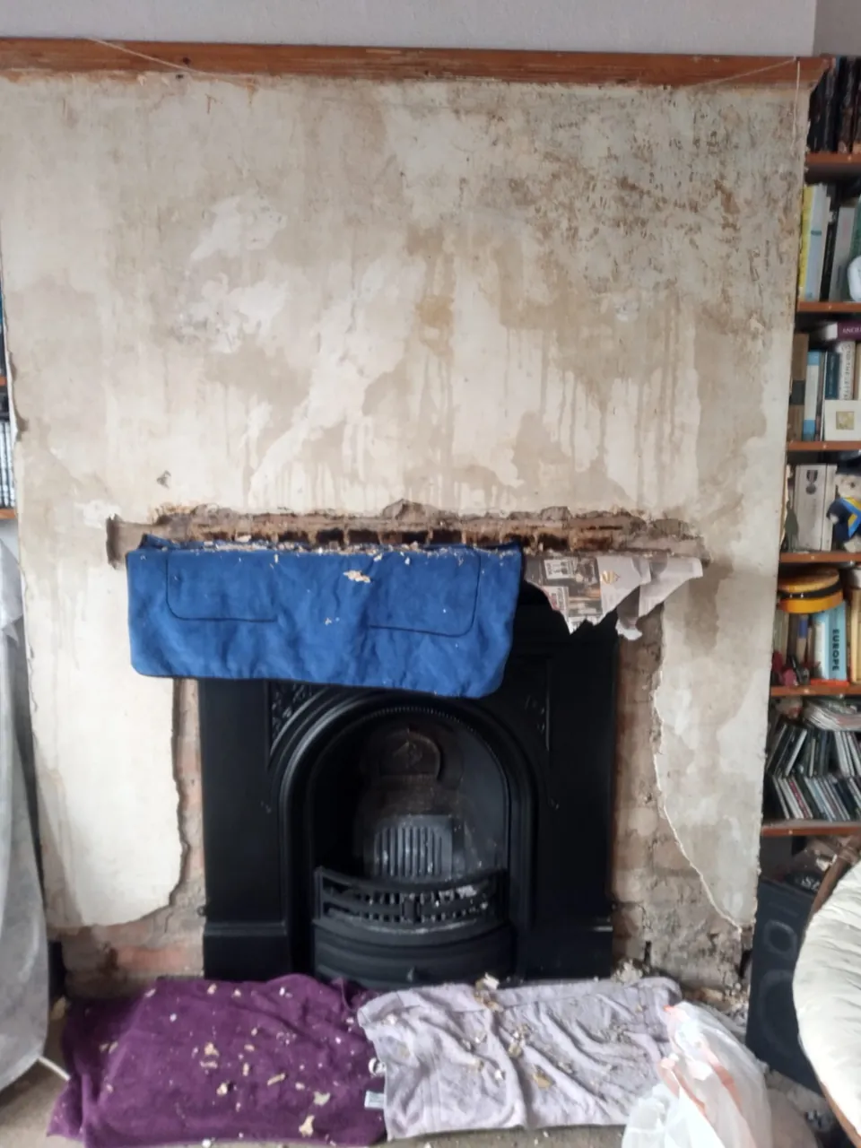 Chimney breast with the old plaster stripped back around a cast iron fireplace, before replastering