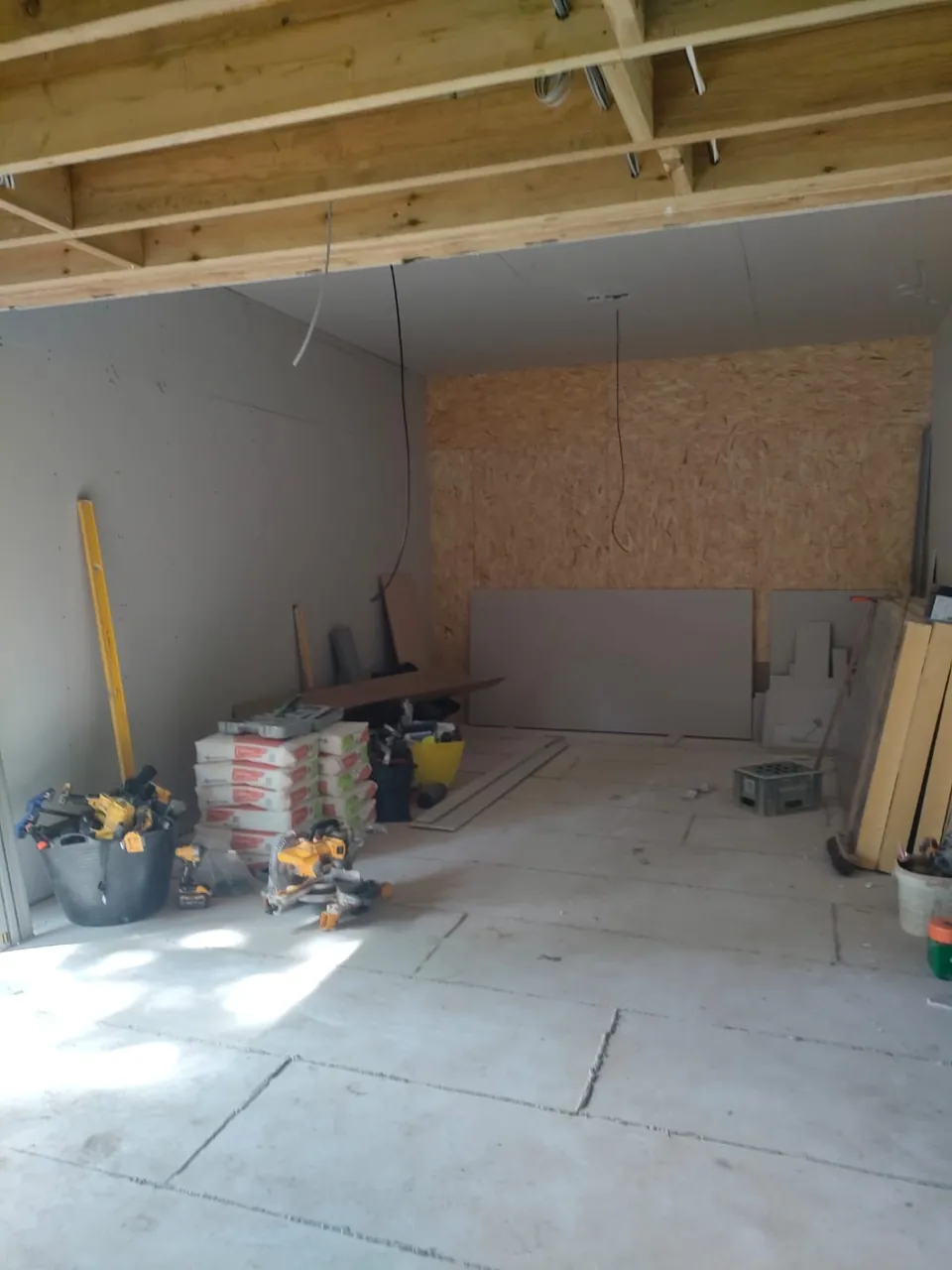 Plasterboarded room with timber joists above, an OSB end wall and boards stacked ready