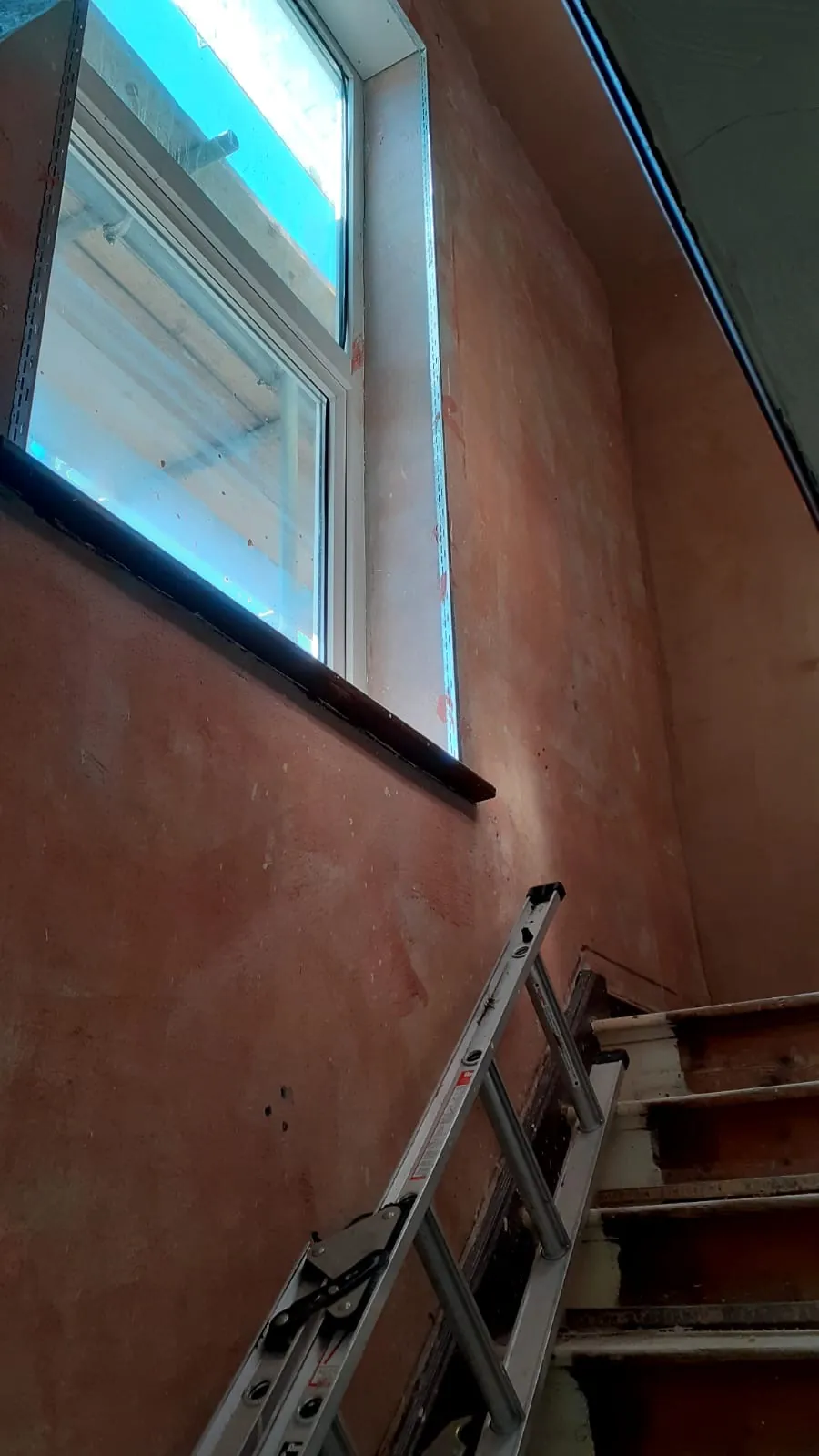 Stairwell wall and window reveal prepared with a bonding coat before plastering, ladder resting on the stairs