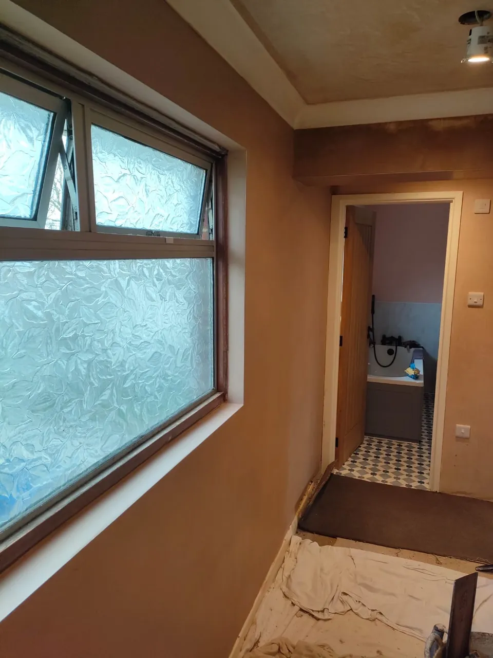 Newly plastered hallway wall and ceiling with a window, and a bathroom visible through the doorway