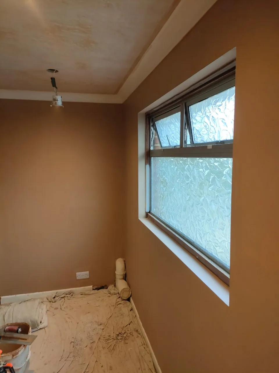 Newly plastered walls with a frosted window and a coved ceiling in a renovated room